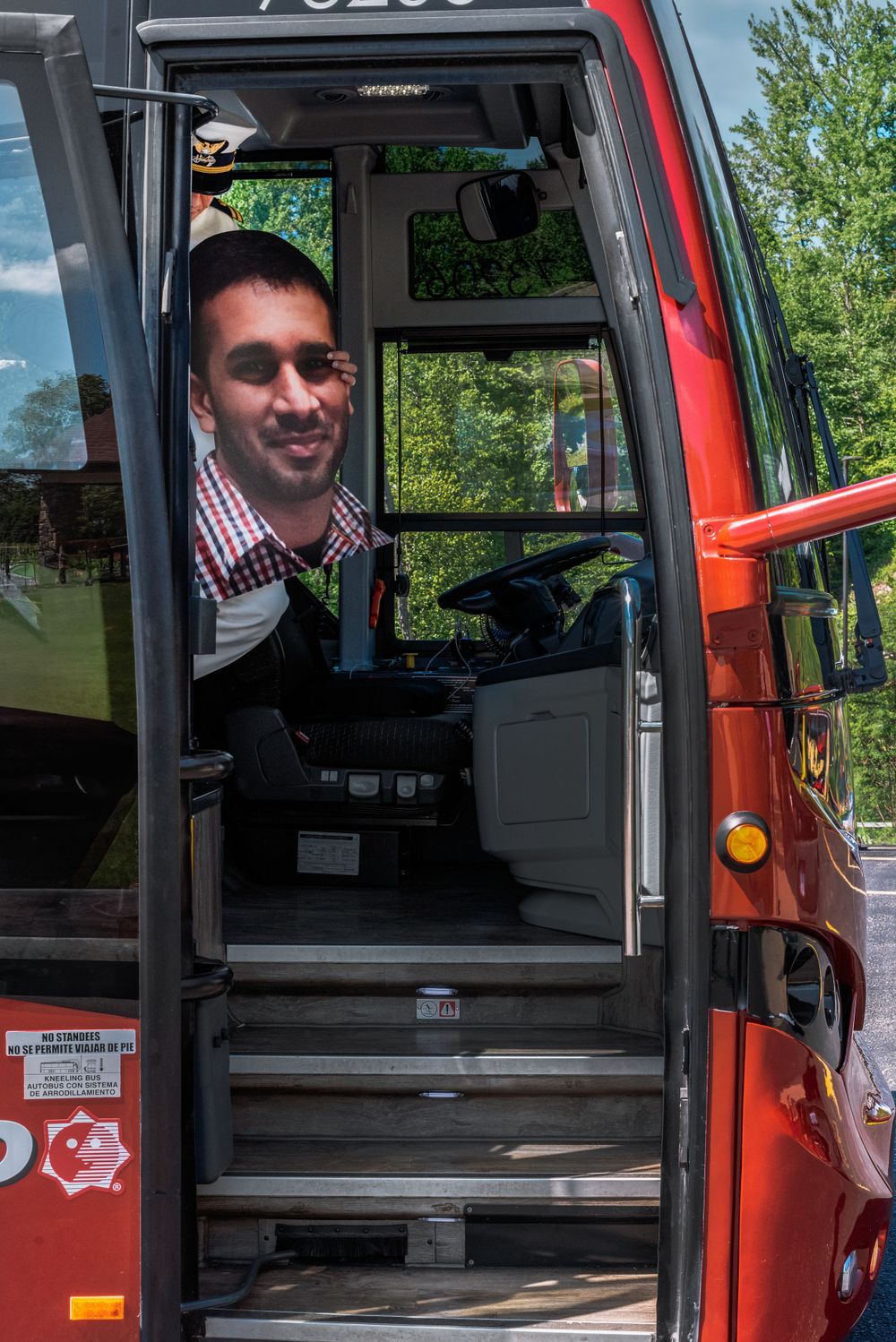 A bus driver smiling from the doorway of a red transit bus.