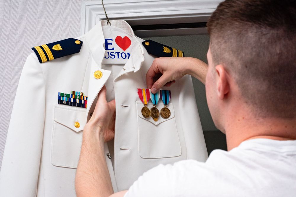 Person placing decorative items on a white military uniform.