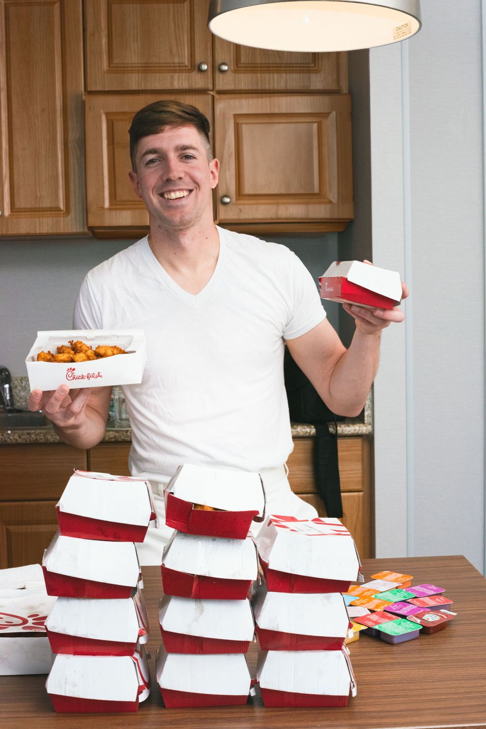 Person holding Chick-fil-A boxes with stacked takeout containers on table.