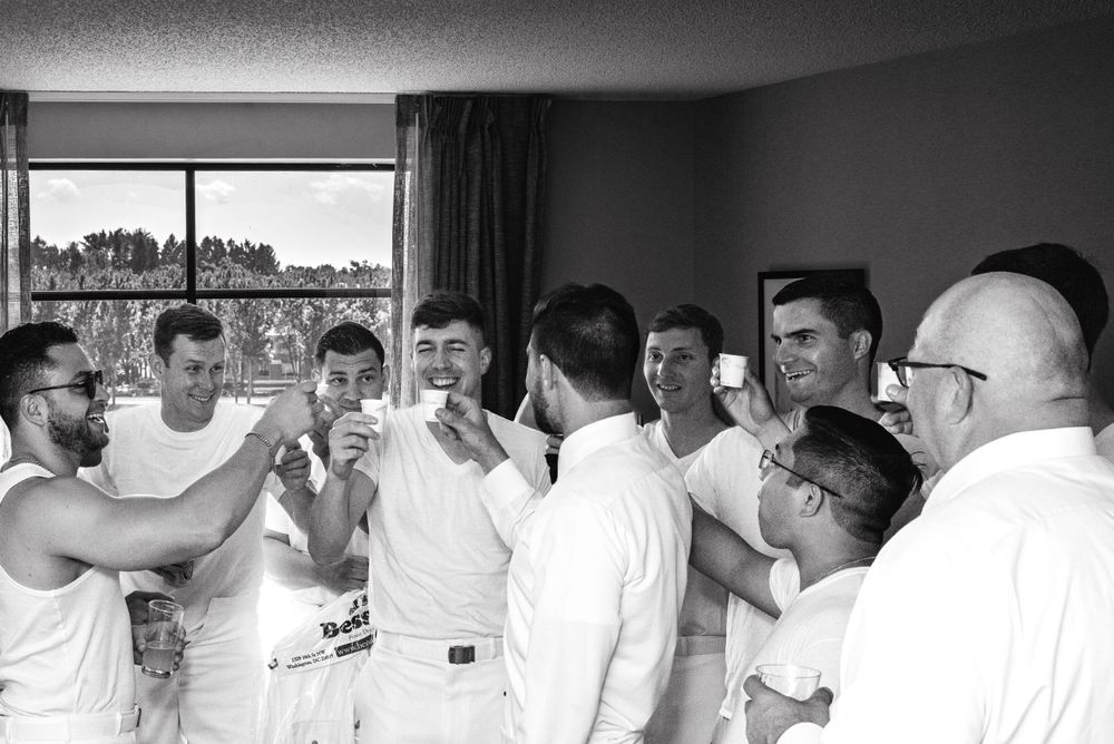 A group of men in white attire gathered in a room toasting with drinks.