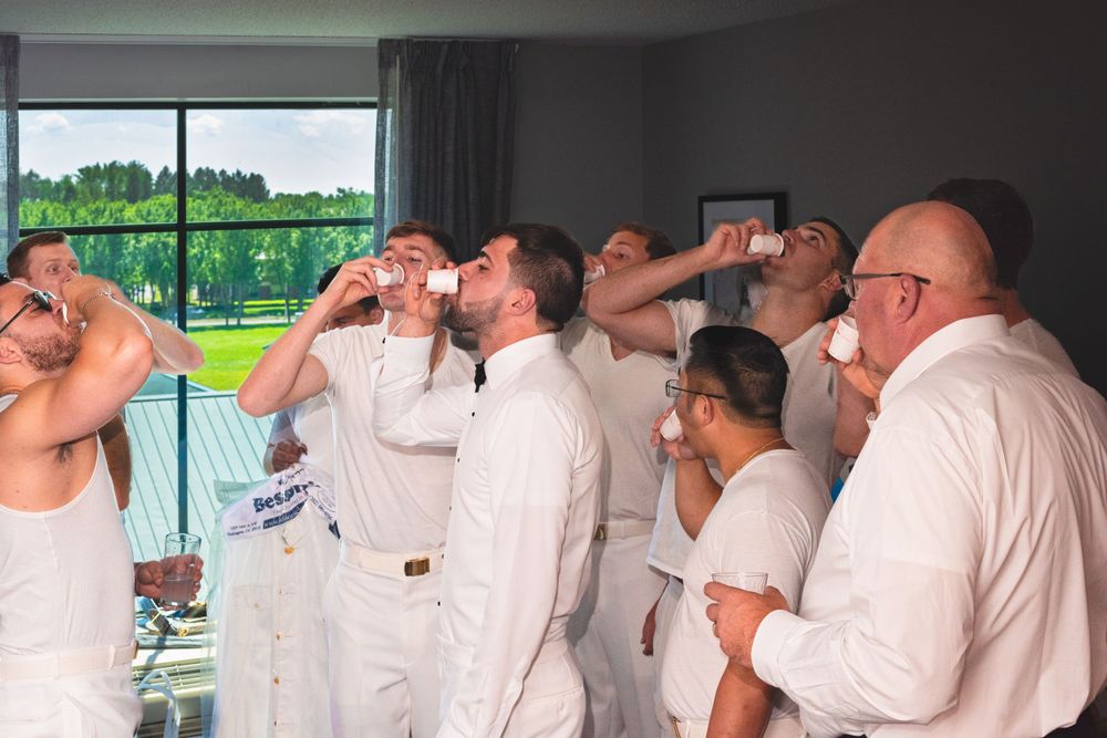 People wearing white clothing taking drinks together in a bright room with windows.