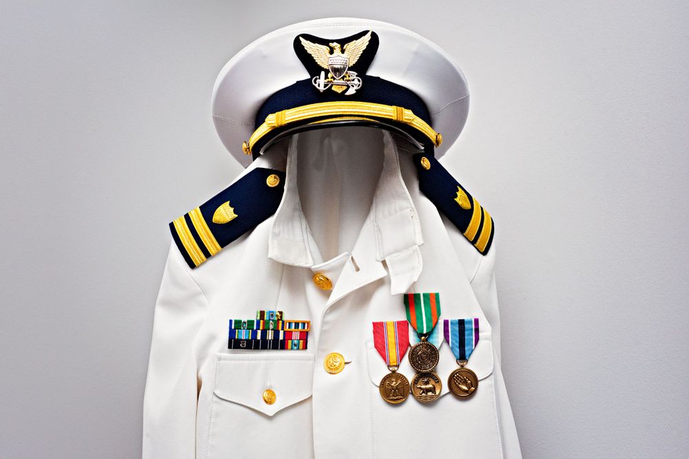 A formal naval dress white uniform with medals and decorations displayed on a hanger.