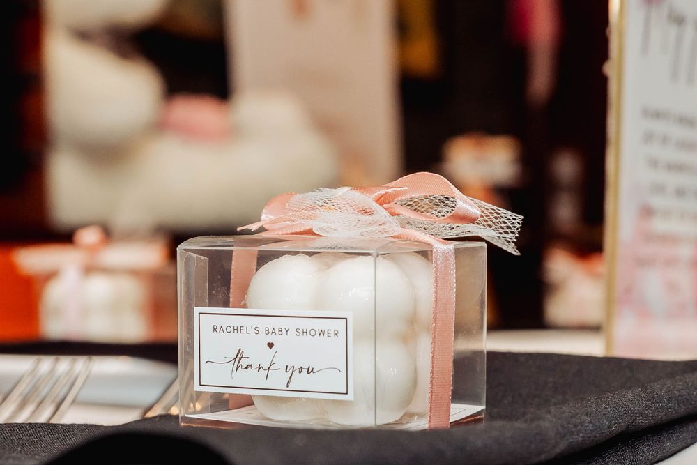 Small pink and white favor box with ribbon displayed on dark surface at a party.