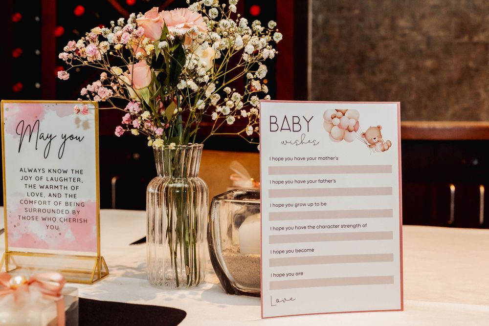 Baby shower decorations featuring floral arrangements and prediction cards on a wooden table.