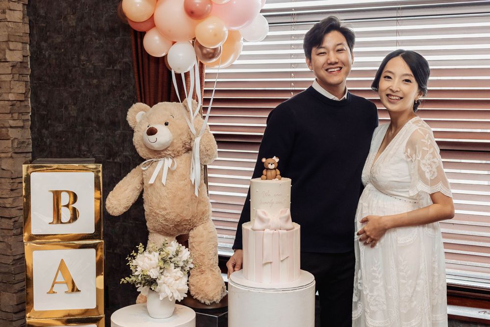 Baby shower setup with balloon arch, teddy bear, wooden blocks, and decorated cake.