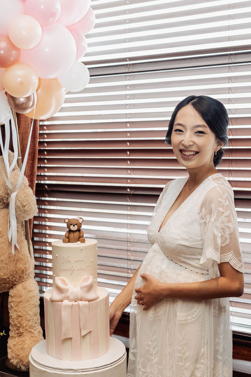 Elegant pink baby shower setup with balloon bouquet, teddy bear cake topper and white lace dress details.