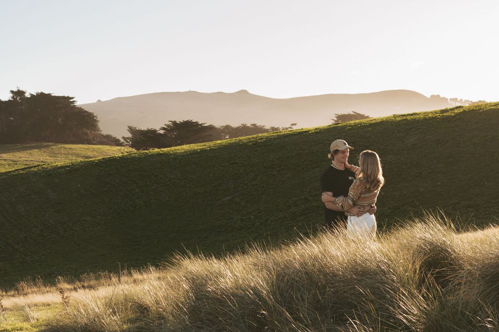 A couple embraces in golden sunlit grass on a hillside.