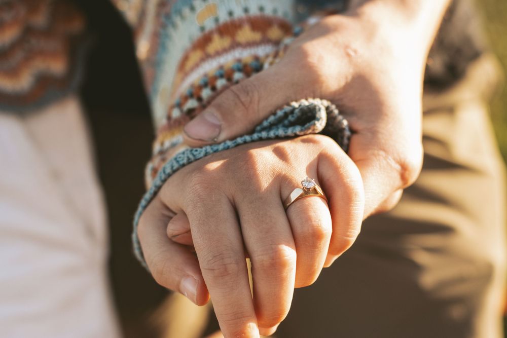 Close-up of intertwined hands wearing colorful bracelets and an engagement ring.