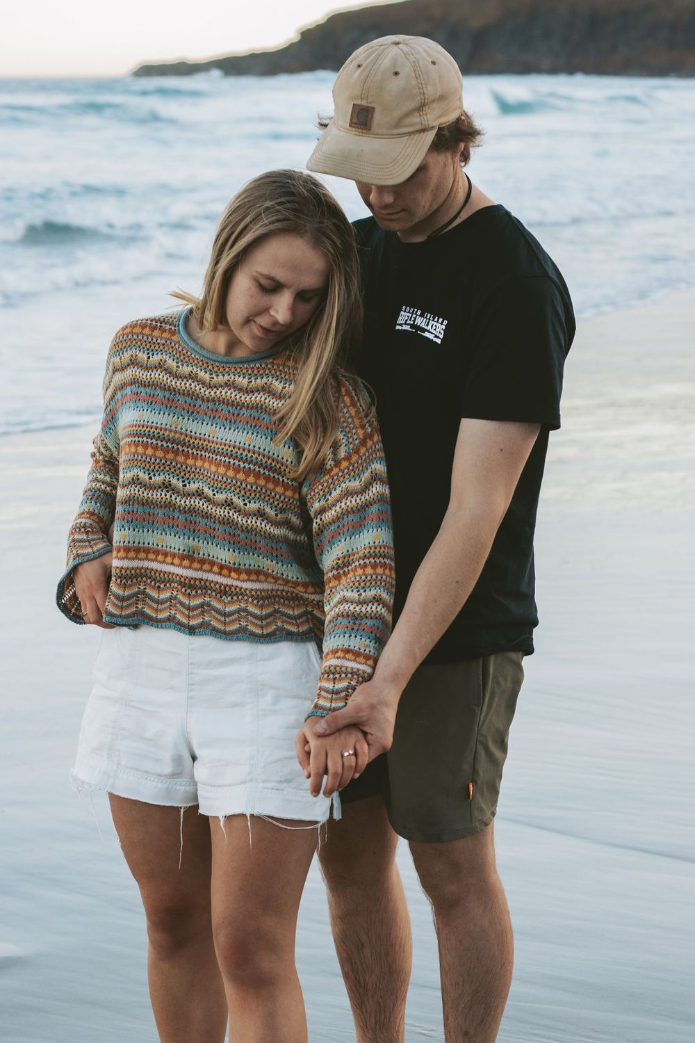 A couple wearing matching sweaters shares an intimate moment on the beach.
