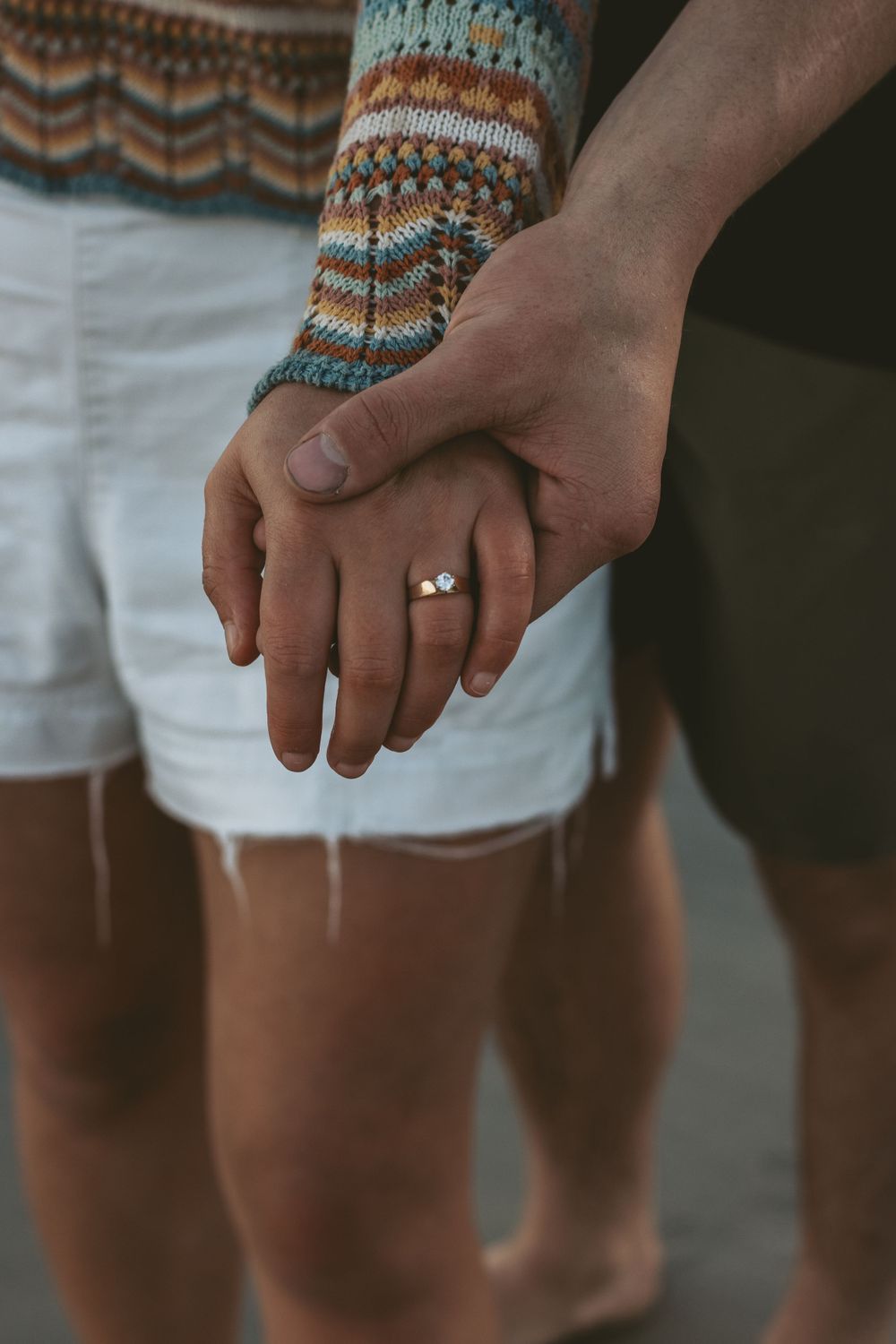 Close-up of intertwined hands with an engagement ring against a knit sweater sleeve.