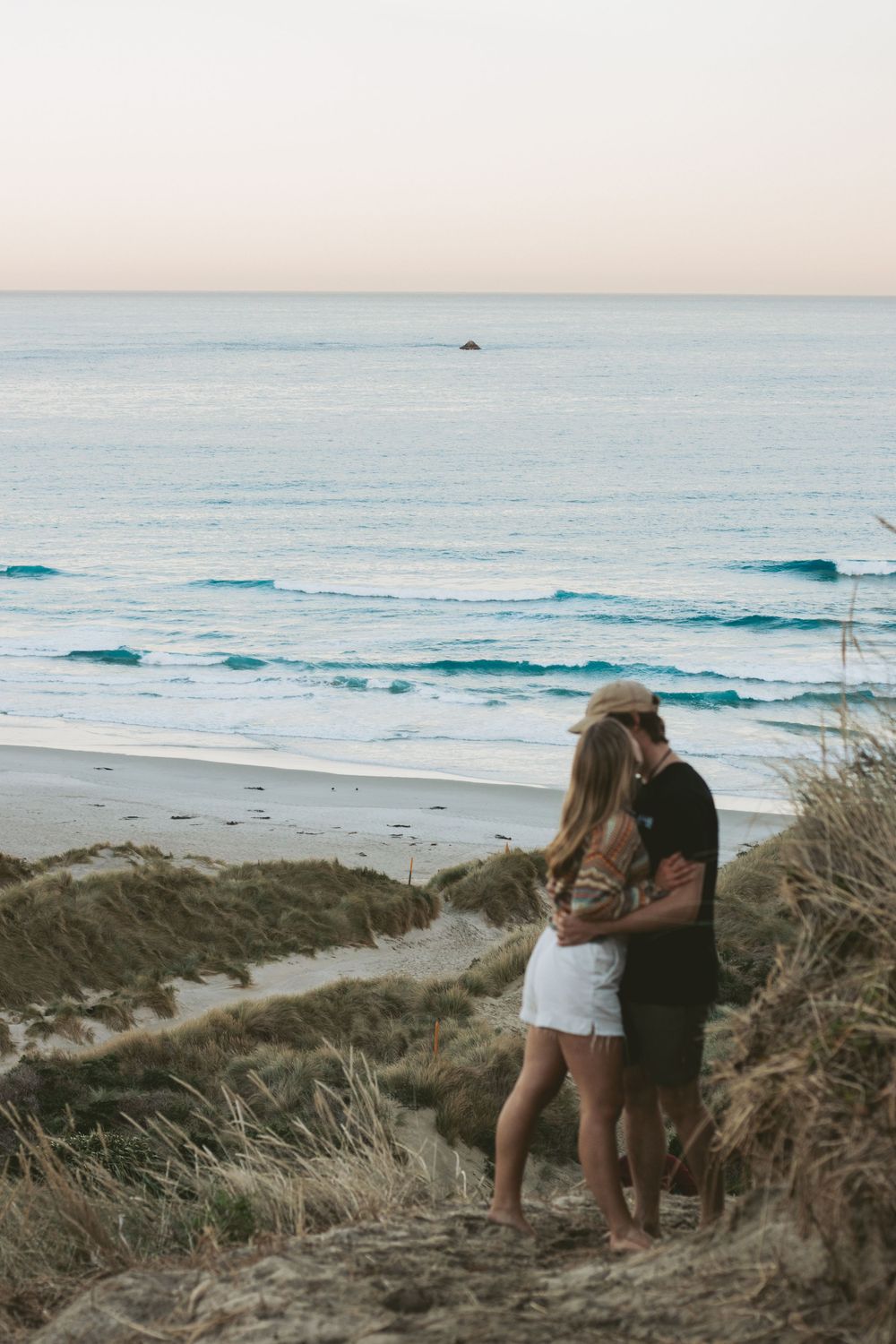 A couple shares an intimate moment on a clifftop overlooking the ocean at dusk.