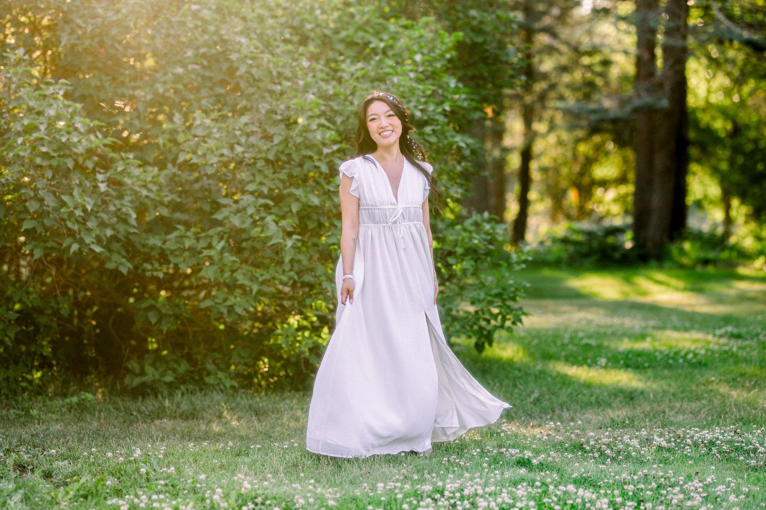 An ethereal portrait in a flowing white dress amid a sunlit forest setting.