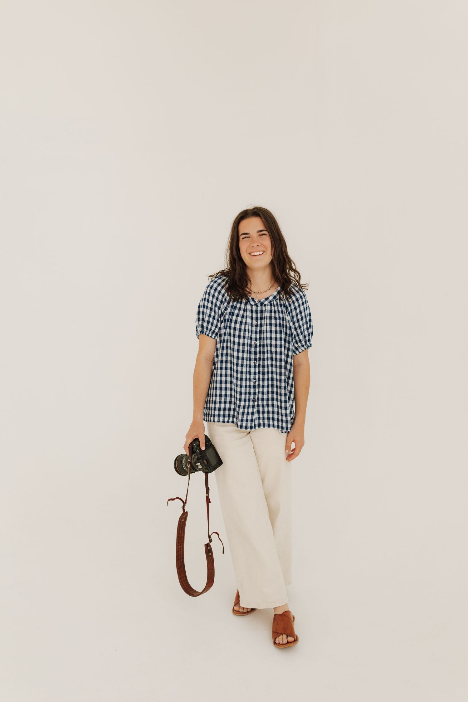 Someone sits cross-legged on a wooden stool in a grassy field at sunset wearing denim overalls and white t-shirt.
