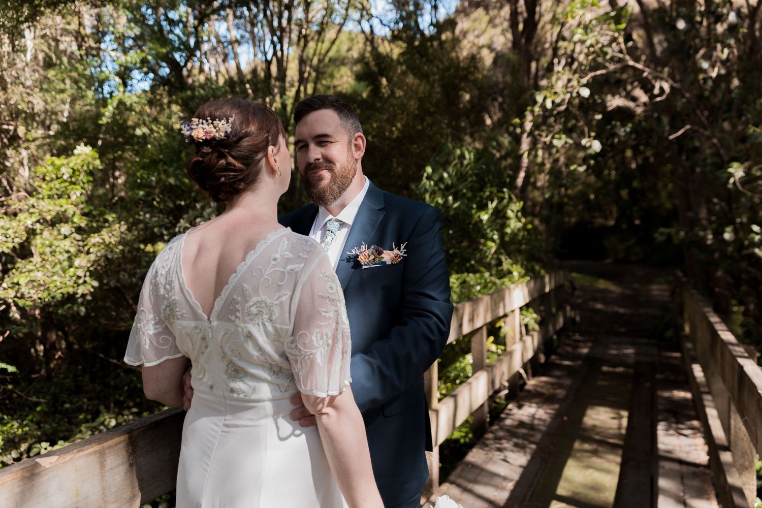 Couple in wedding attire share a tender moment on wooden bridge.