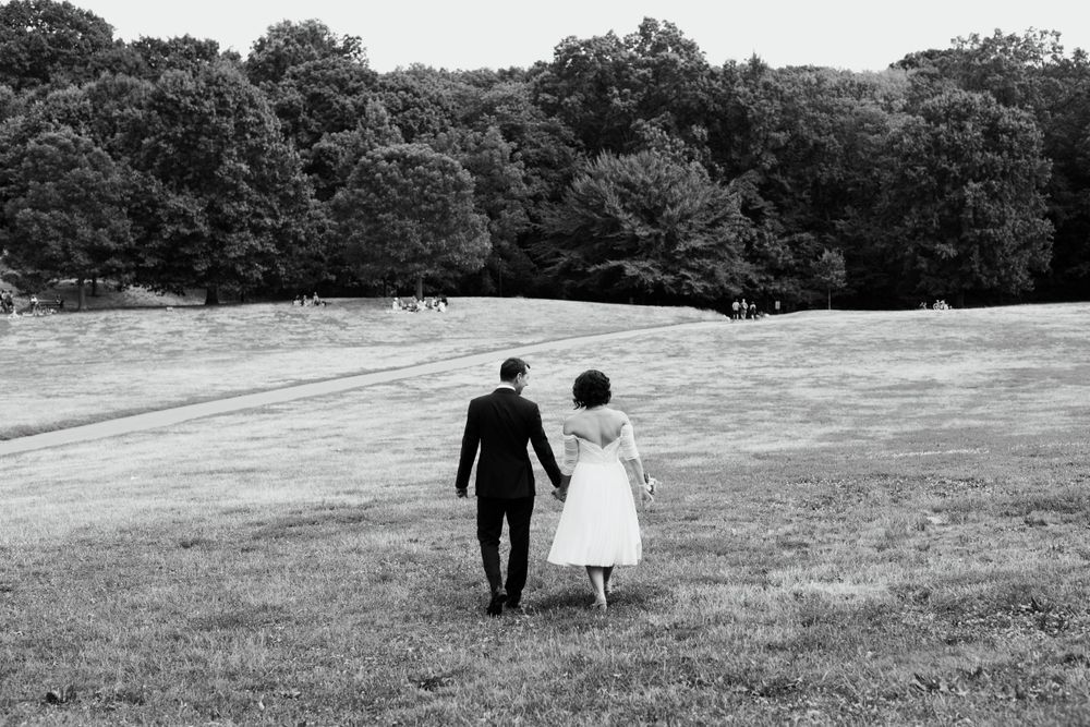 A black and white photo of newlyweds walking hand in hand across a scenic hillside.