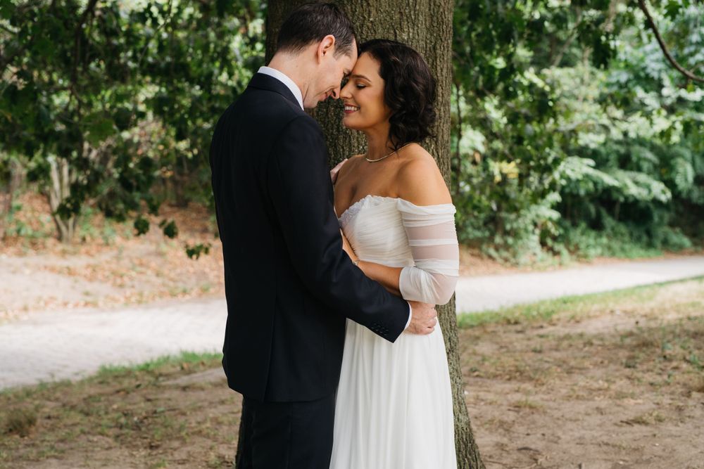 A romantic moment between newlyweds embracing under a tree in an outdoor setting.