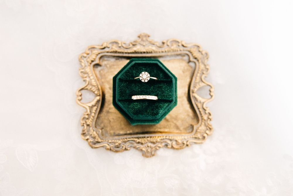 An engagement ring displayed in an ornate vintage gold frame with dark green velvet interior.