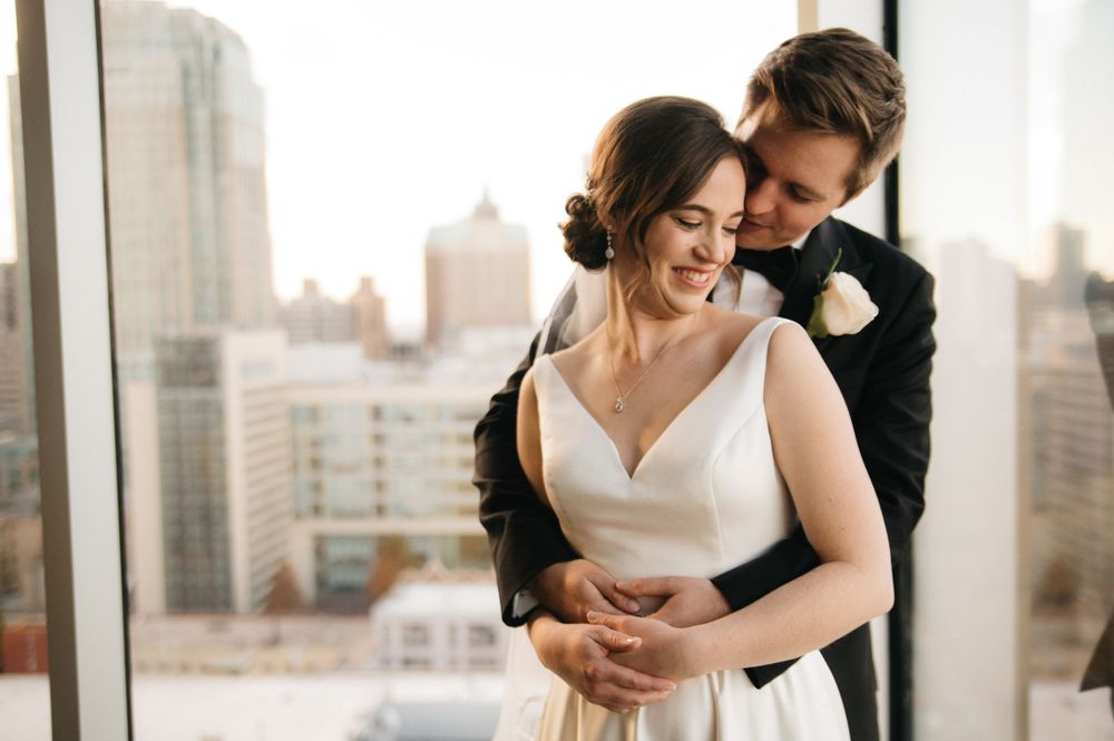 A tender moment between newlyweds against a cityscape backdrop at sunset.
