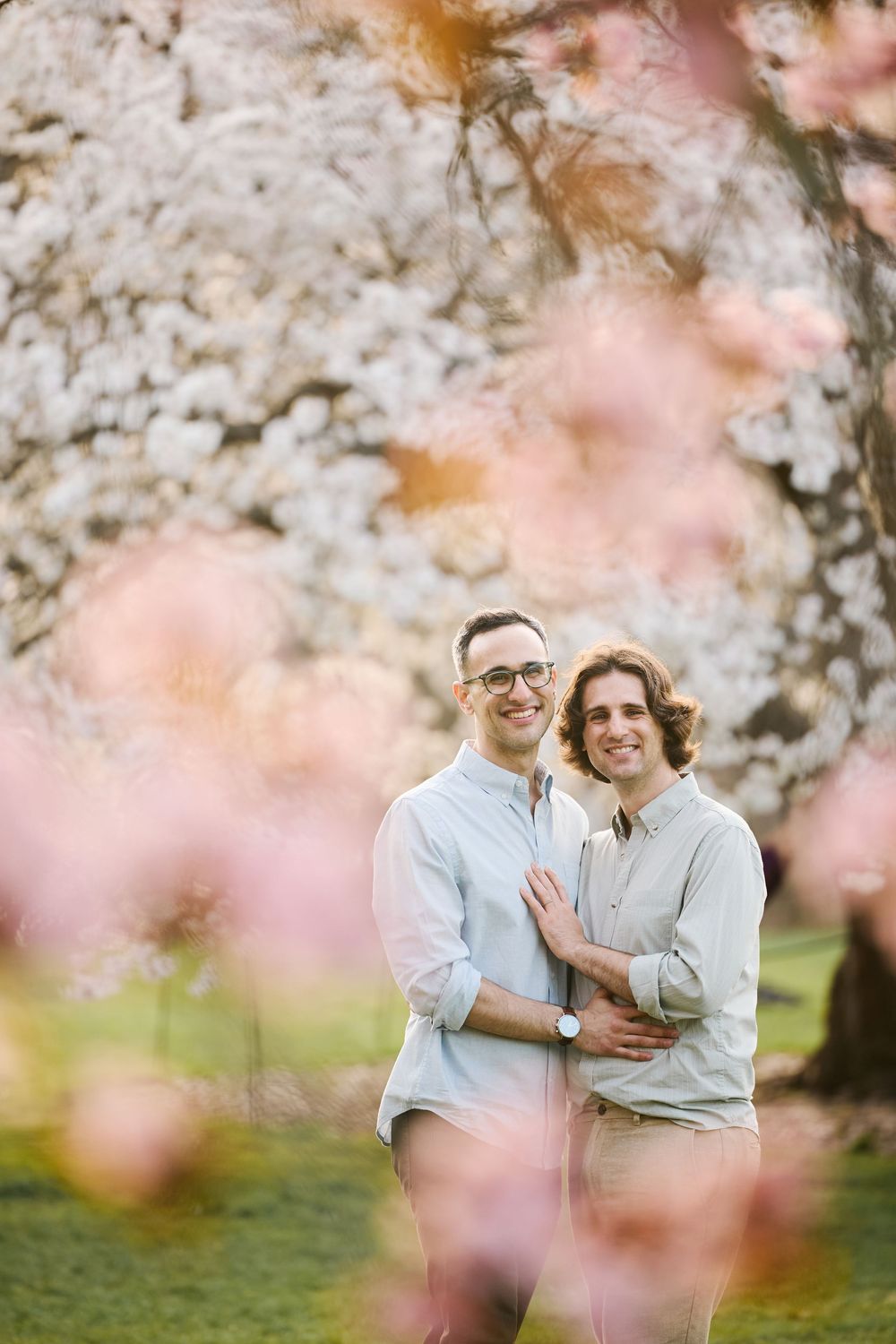 A romantic spring portrait framed by soft pink cherry blossoms in bloom with a natural dreamy bokeh effect.