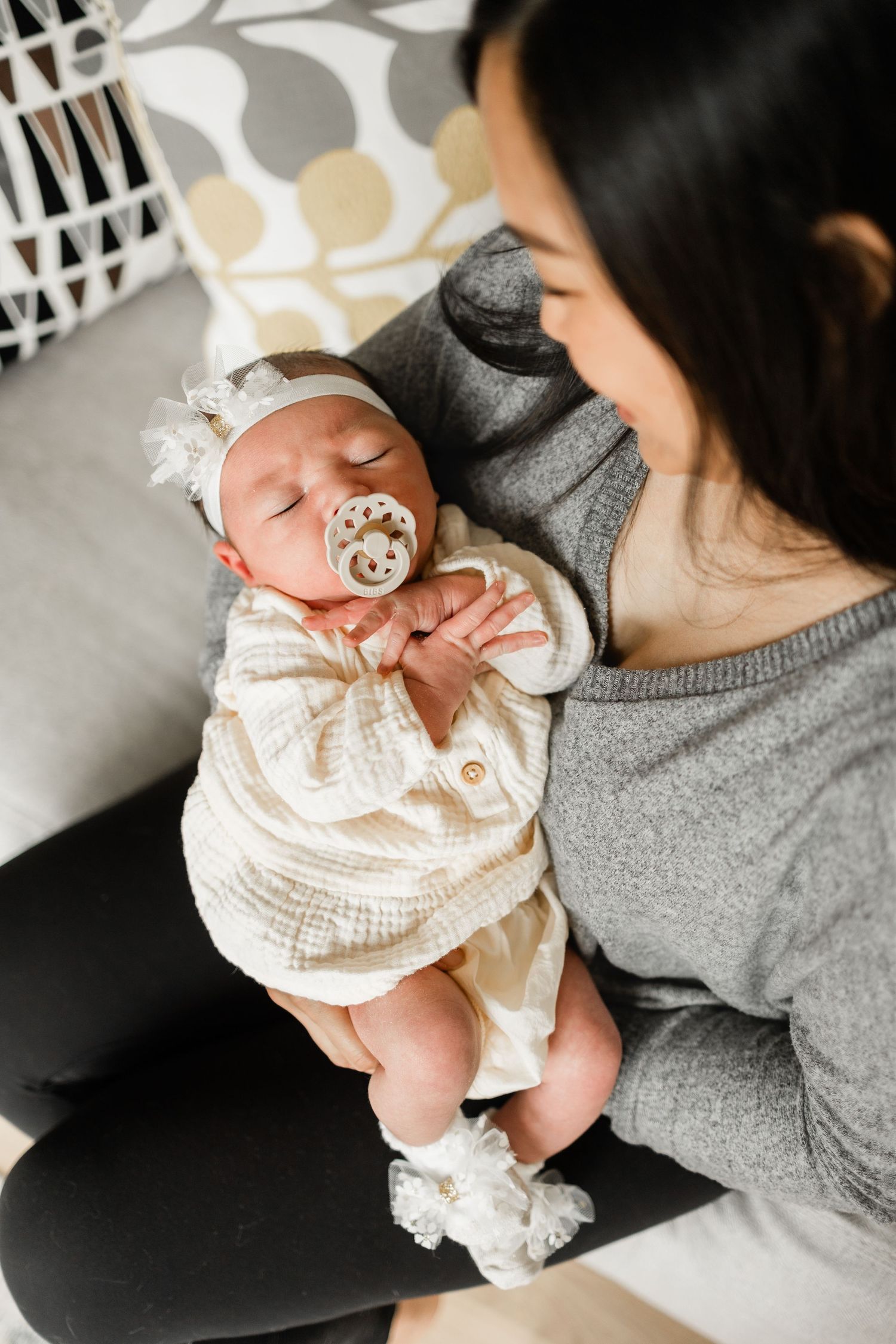 A newborn baby in a cream-colored outfit rests peacefully with a pacifier while being cradled.