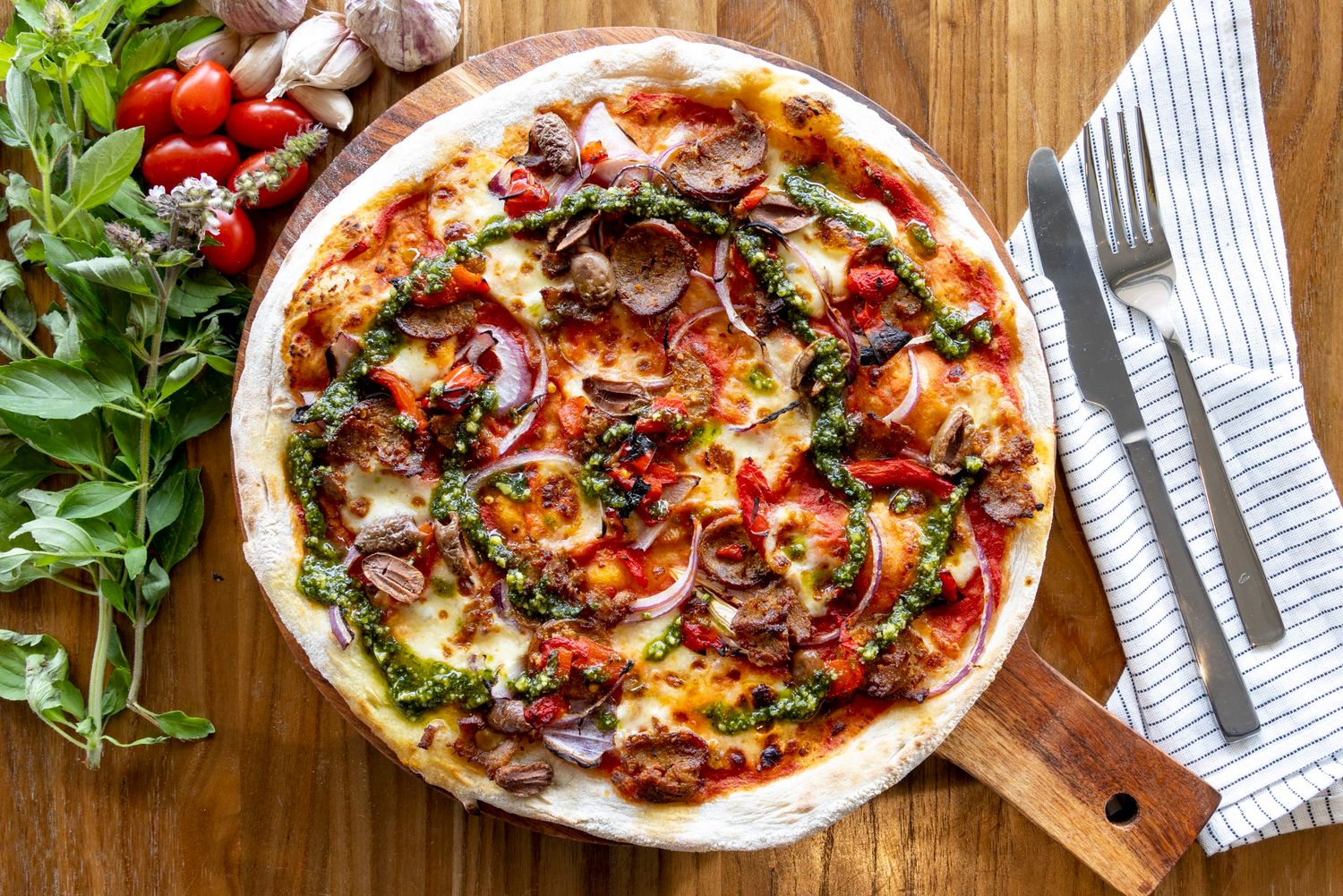Rustic pizza topped with mushrooms, pepperoni and fresh herbs on wooden board.