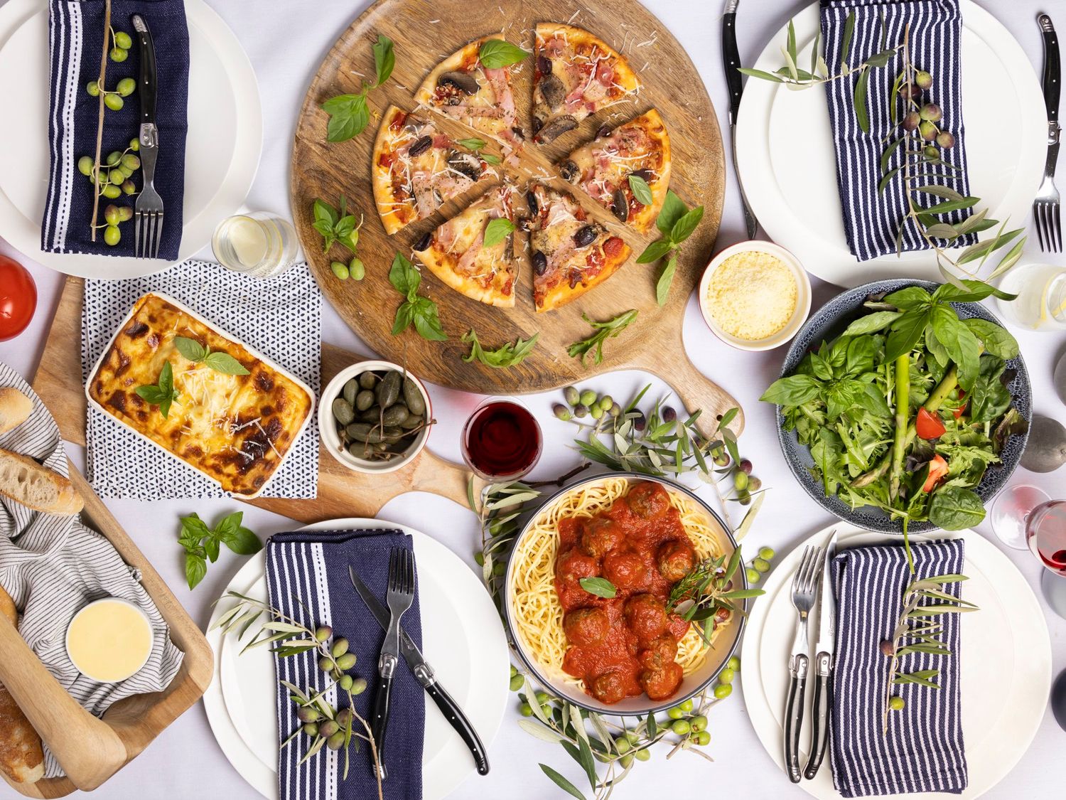 Overhead view of an elegant dinner table with pizza, meatballs, salad and striped napkins.
