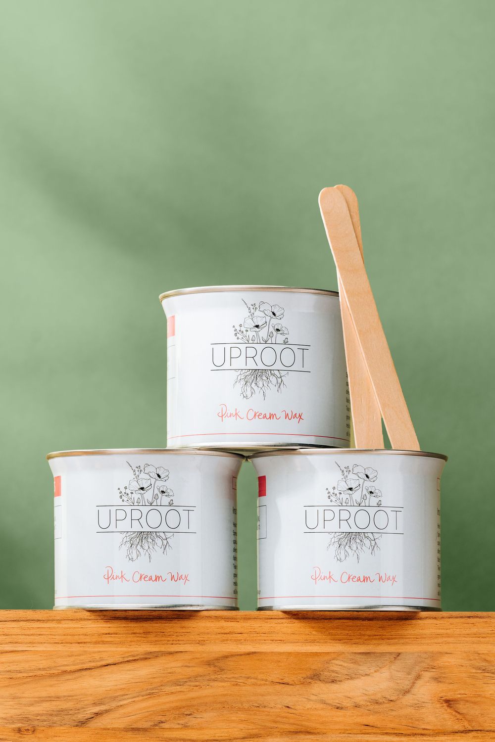 Three stacked white Uproot branded cans with wooden spoon on wooden surface against green background.