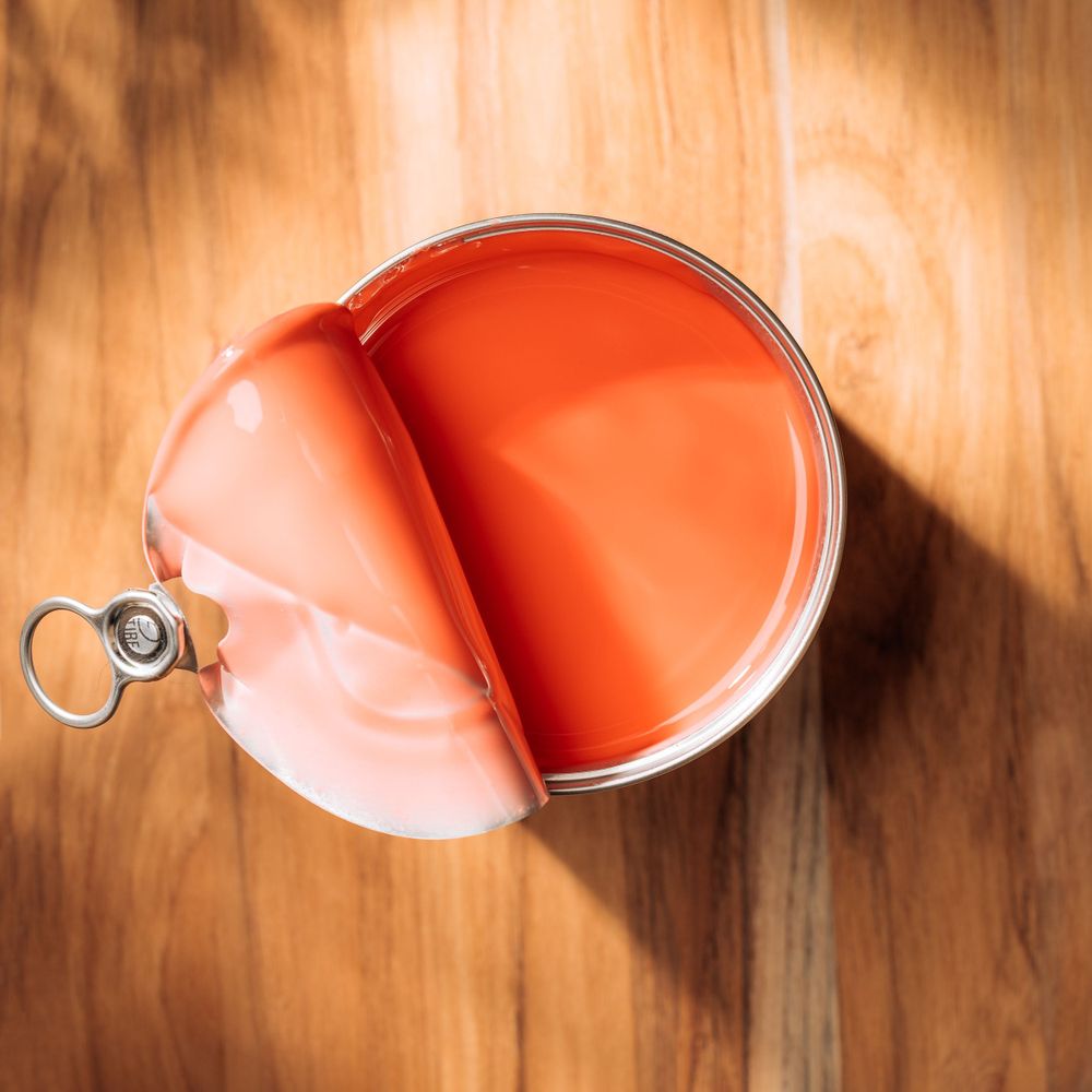 Top view of opened paint can showing bright orange paint with pull tab.