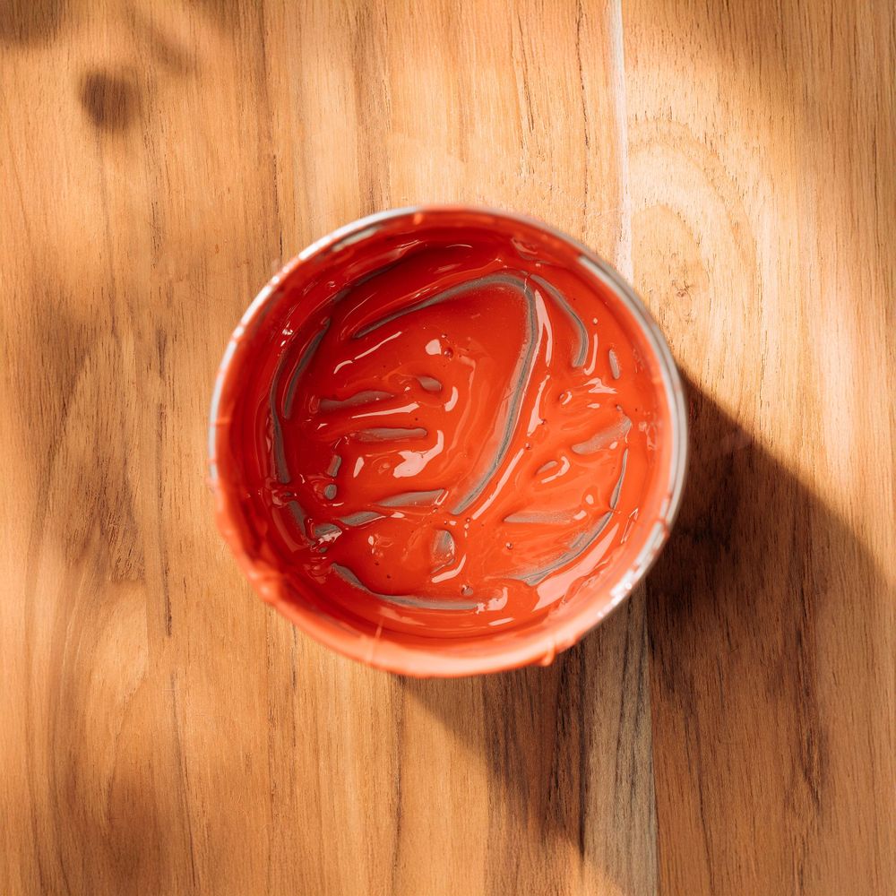 Overhead view of opened paint can containing vibrant red-orange paint with swirl patterns.