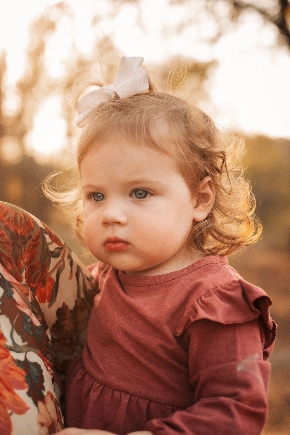 A dreamy sunset portrait in warm autumn tones showing a small figure in burgundy with a white bow.