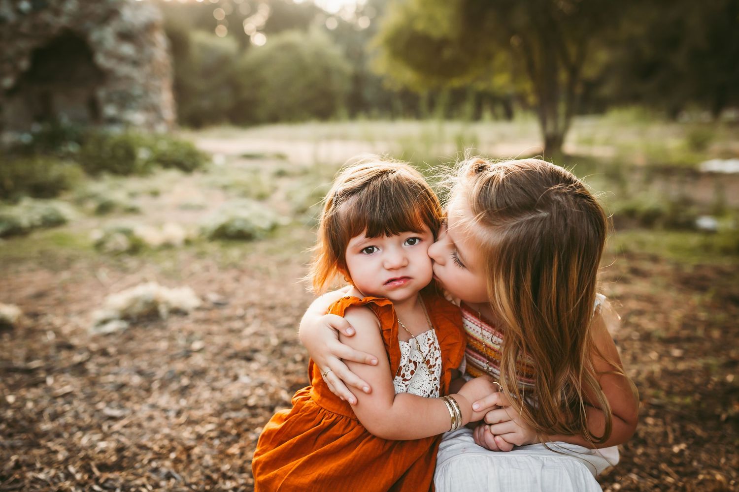 In a natural outdoor setting lit by golden sunlight, a tender moment is shared between two family members.