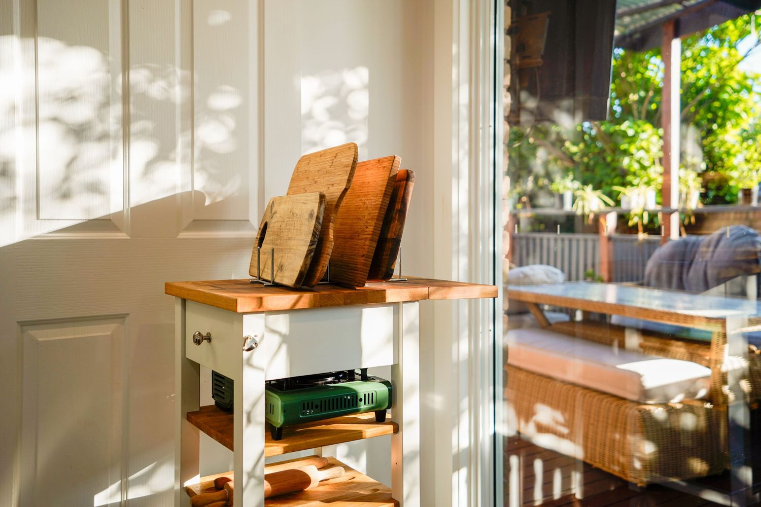 Wooden shelving unit with stacked items in sunlit room with porch seating visible.