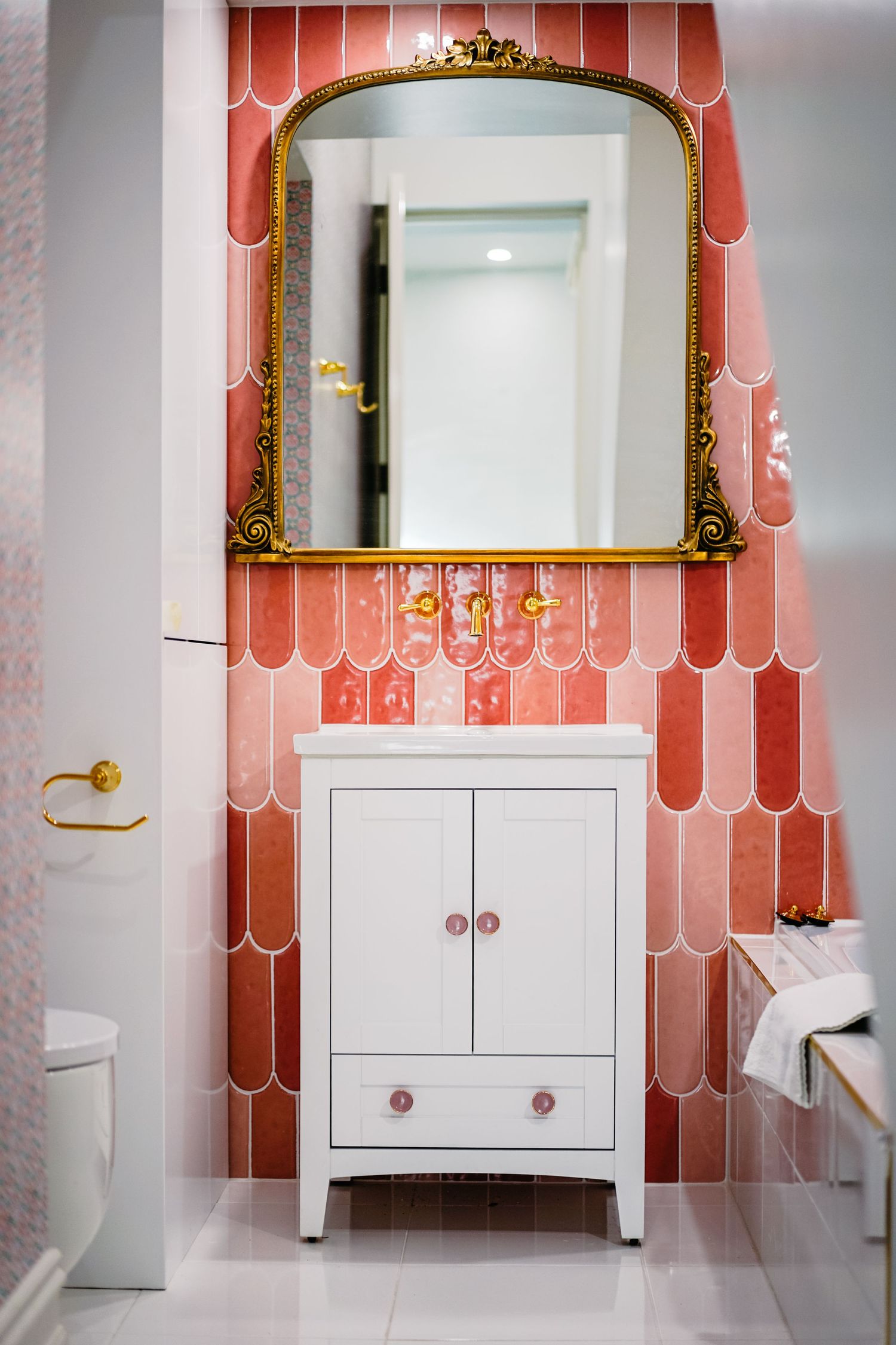 Pink scalloped tile bathroom with ornate gold mirror and white vanity cabinet.