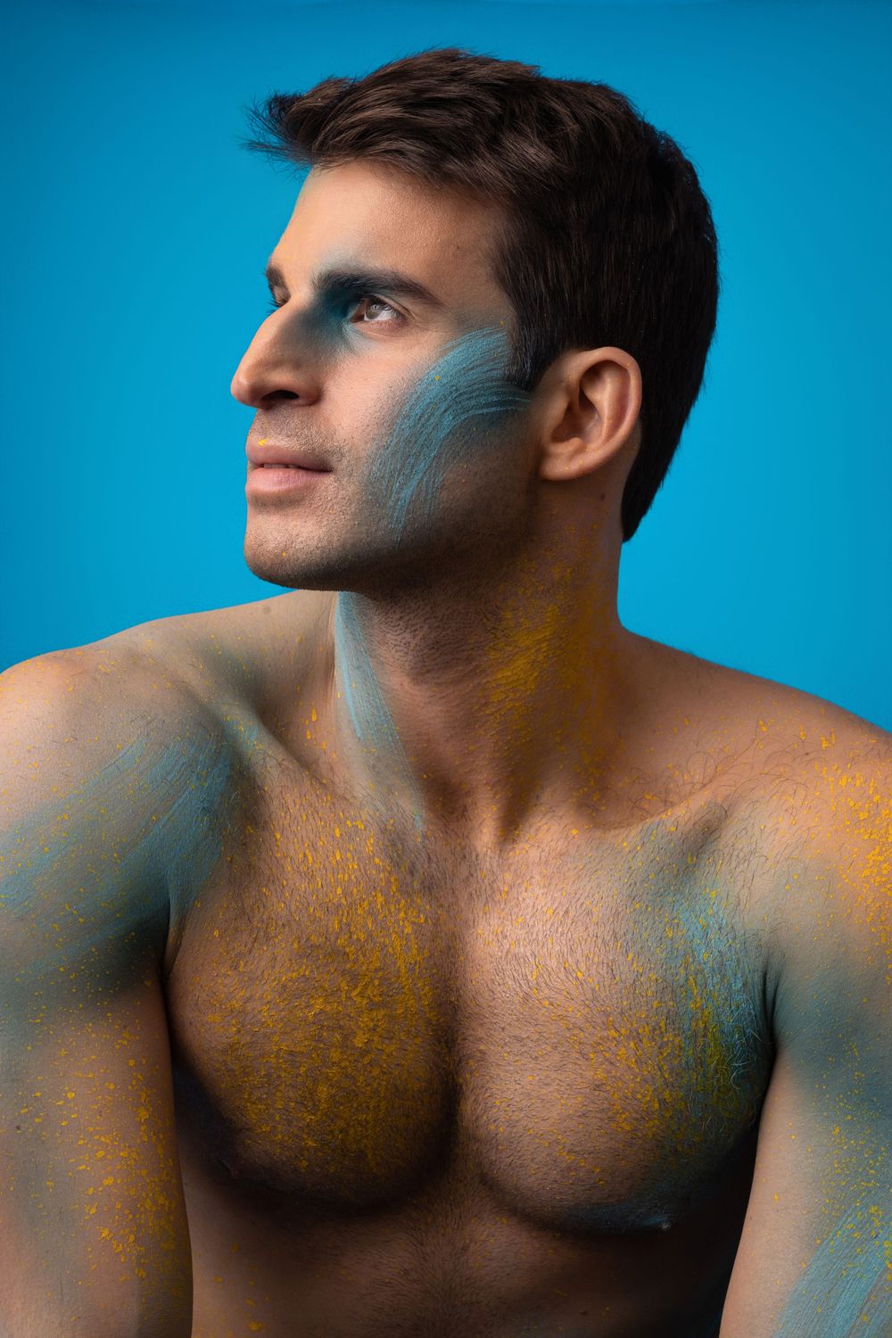 Artistic portrait with blue and orange paint accents on torso against vivid blue background.