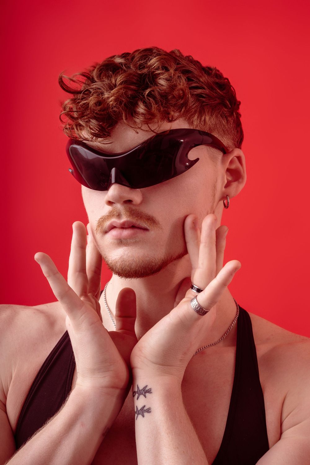 Modern fashion portrait of someone wearing dark sunglasses and black top against vibrant red background.