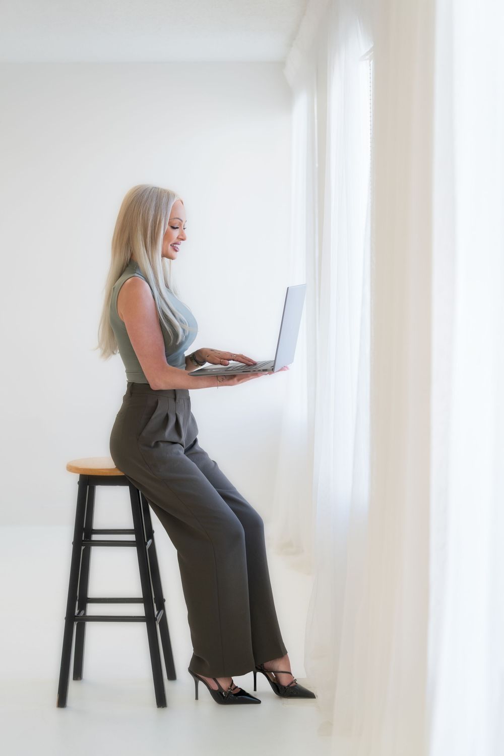 Professional lifestyle photo showing standing pose at stool with laptop in bright minimal white setting.