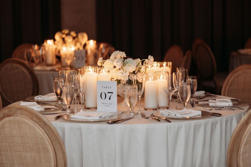 Elegant round wedding reception table with white linens, glowing candles and floral centerpiece displaying table number 07.