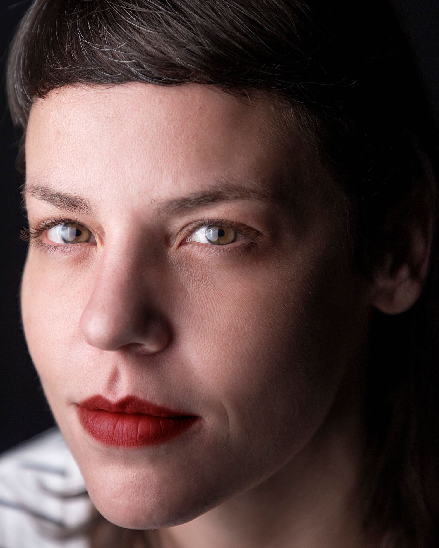 A close-up portrait with red lips and short dark hair against a dark background, creating a dramatic contrast.