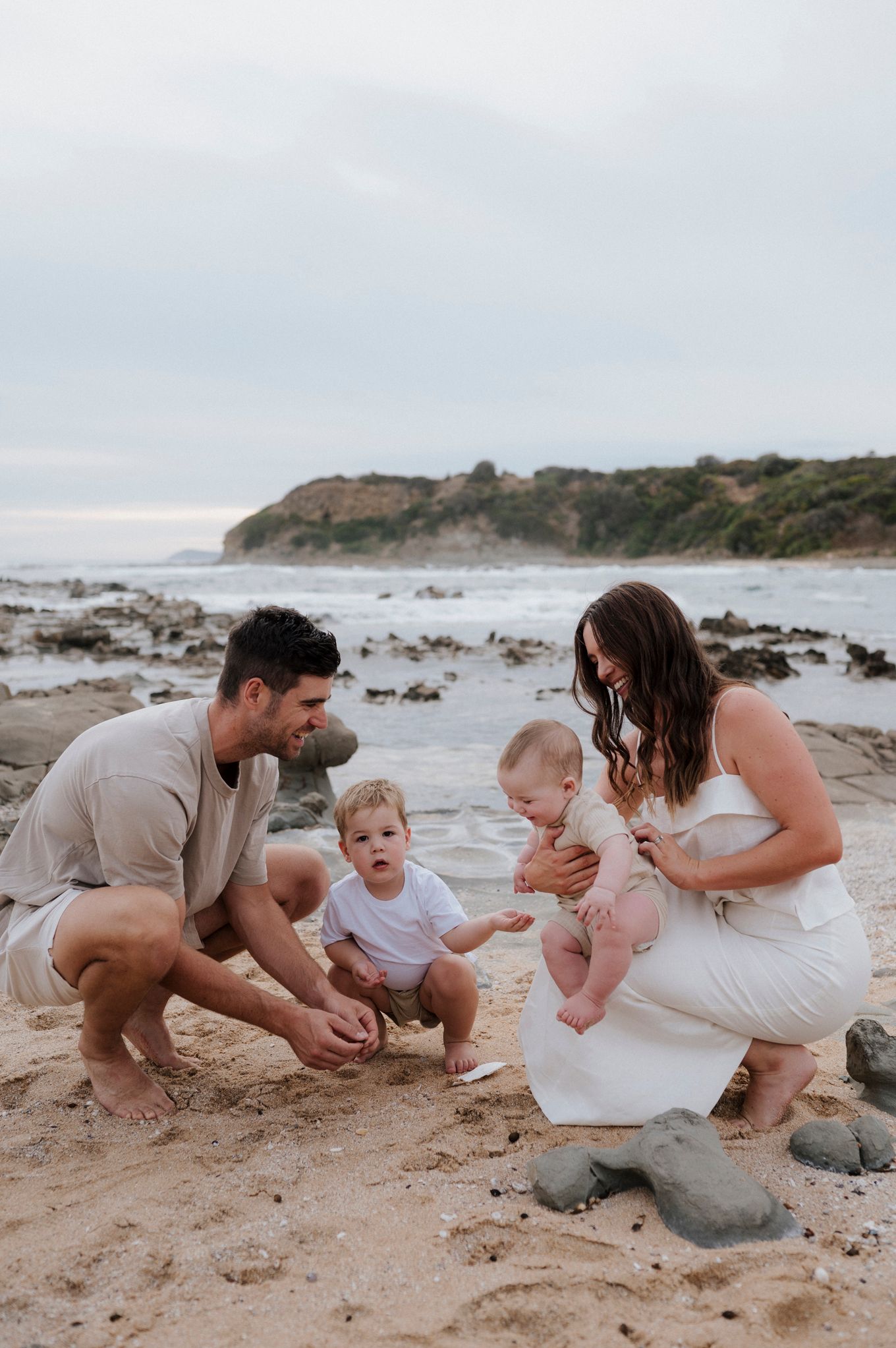 Family playing together on a rocky beach with coastal cliffs in background.