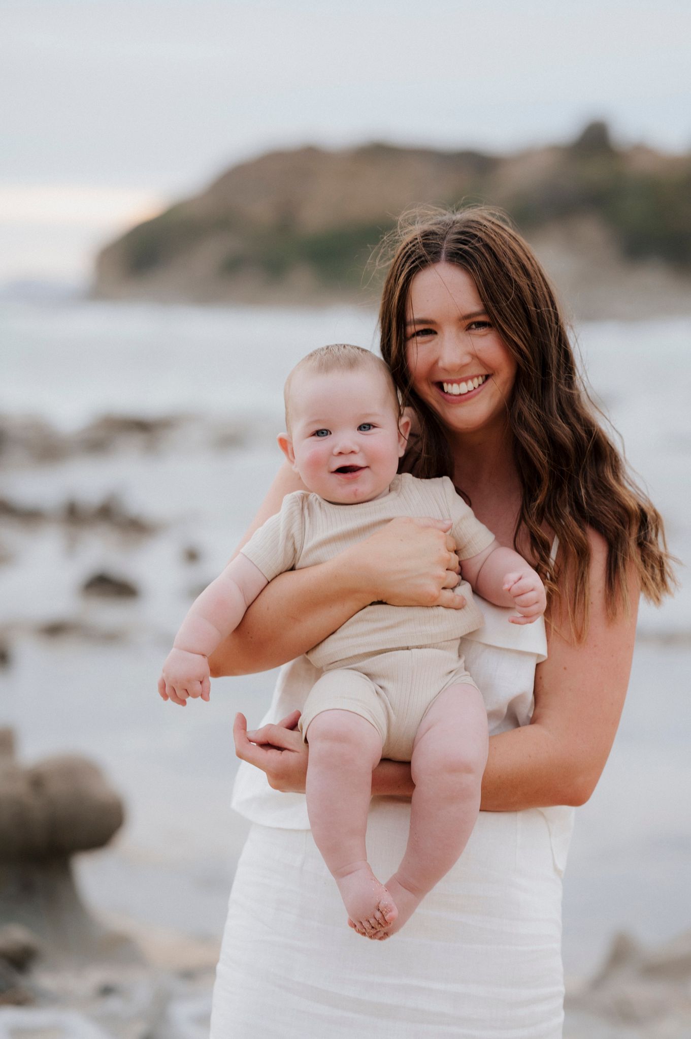 Mother and baby enjoying a sunny day at a rocky coastal beach.