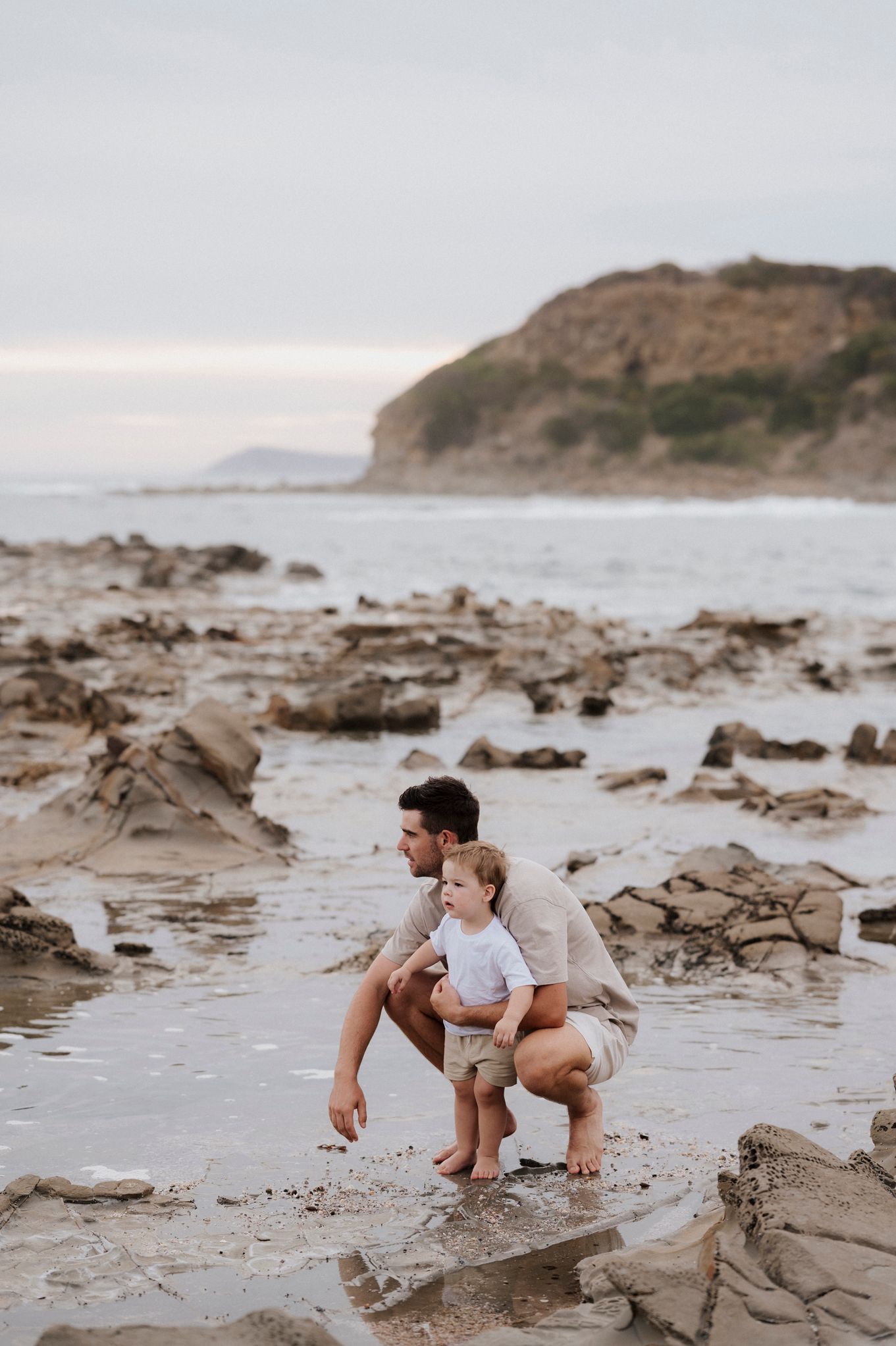 Adult and child exploring rocky beach together near coastal cliffs.