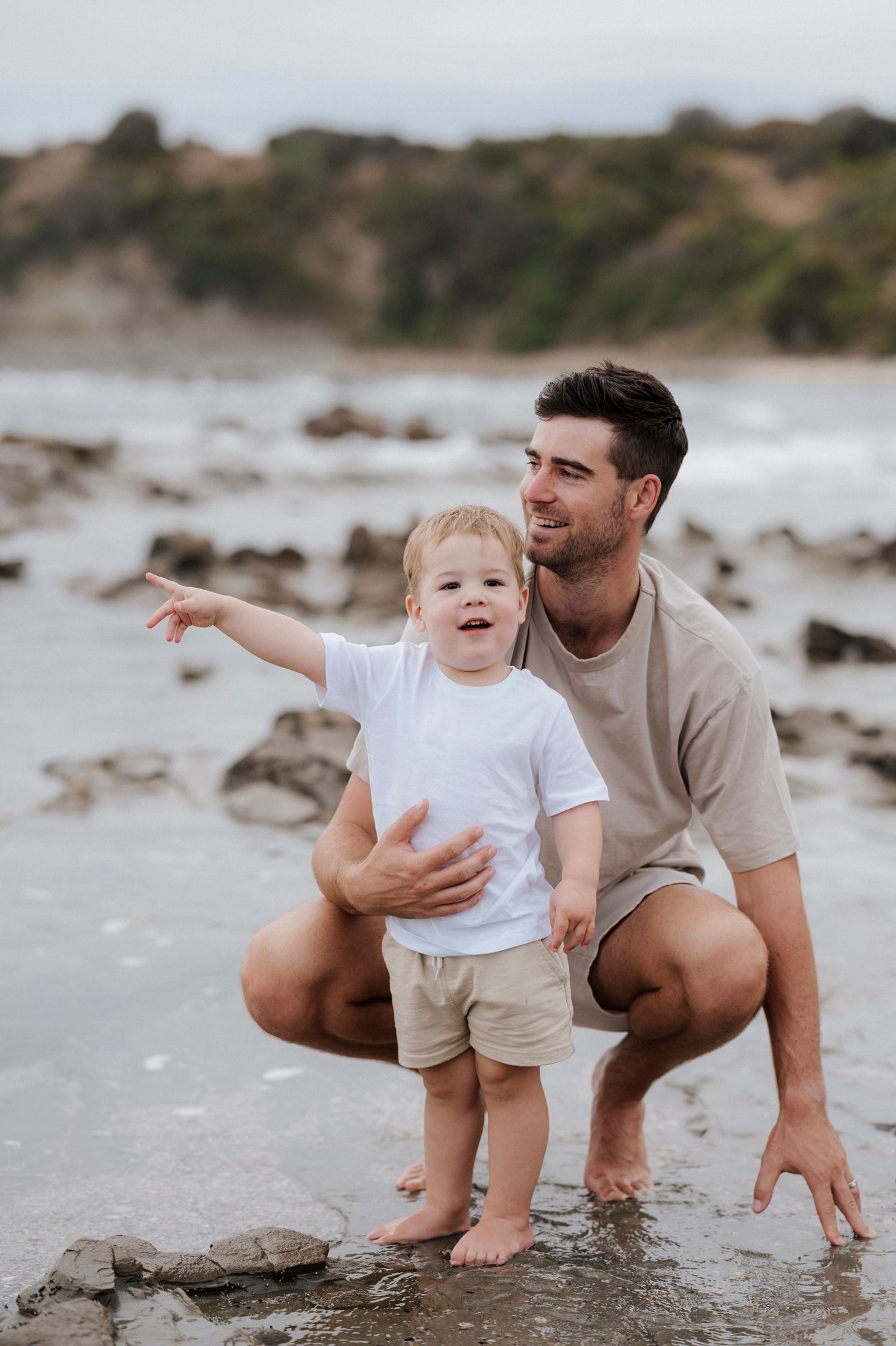 Parent and toddler discover beach treasures while pointing at something in distance.