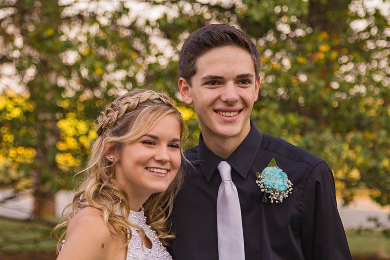 Formal couple poses outdoors against autumn foliage background.
