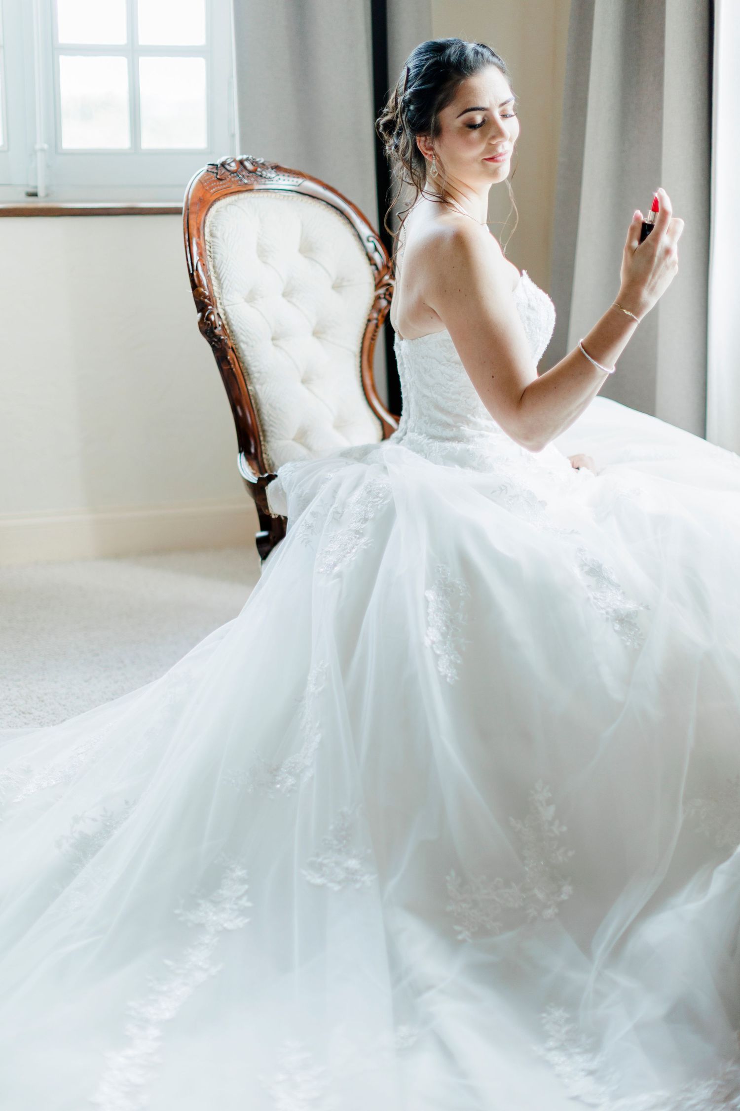 Wedding dress detail shot featuring an elegant white gown on an antique tufted chair.