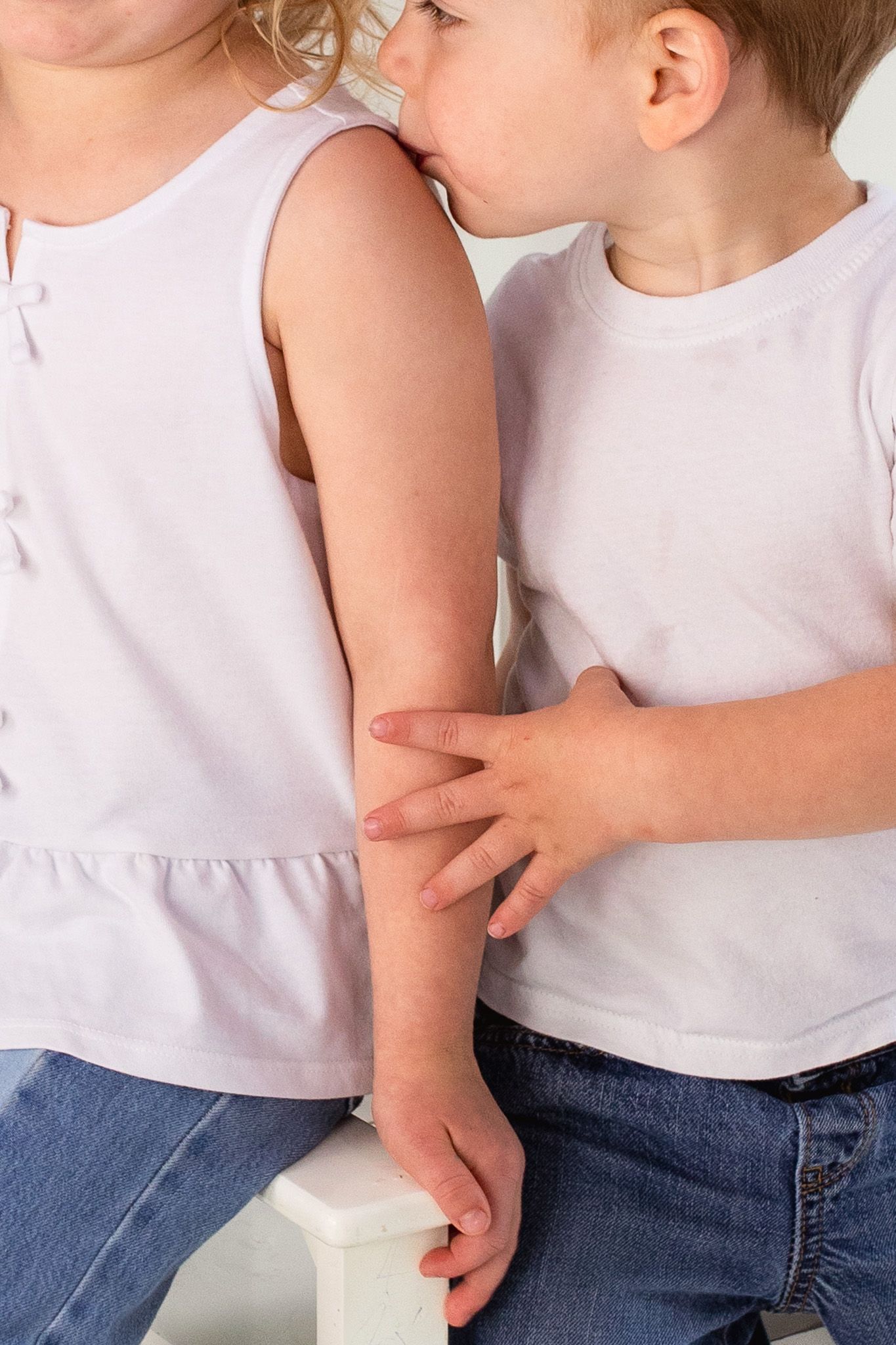 Close-up view of two young children in white shirts and jeans holding arms together.