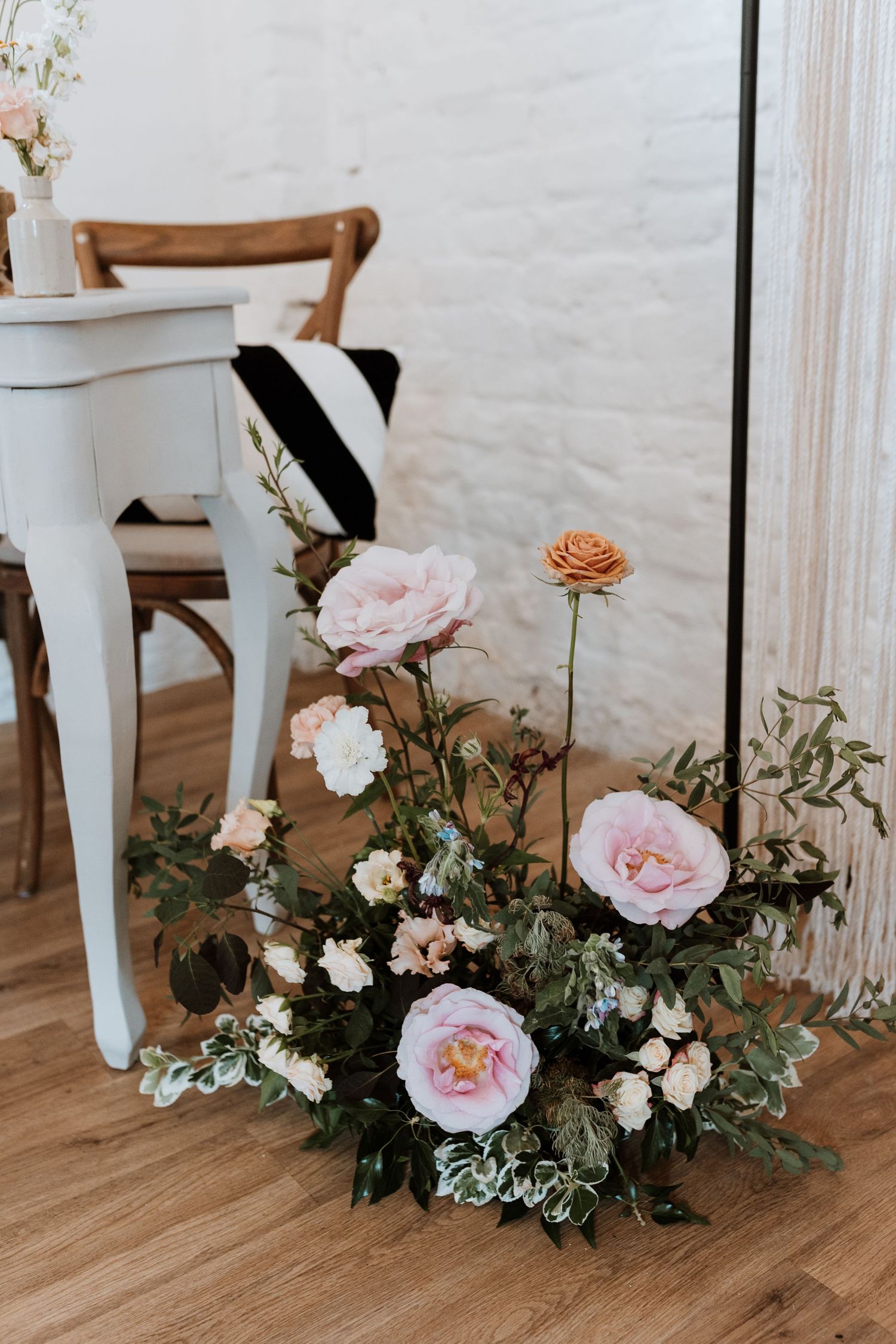 Beautiful flower arrangement with pink roses and eucalyptus next to a white piano leg on hardwood flooring.