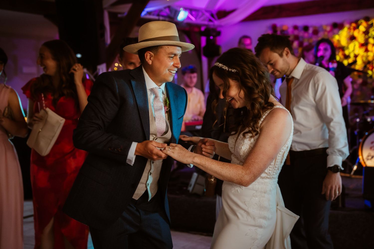 A couple shares a joyful dance moment under warm hanging lights at their wedding reception.