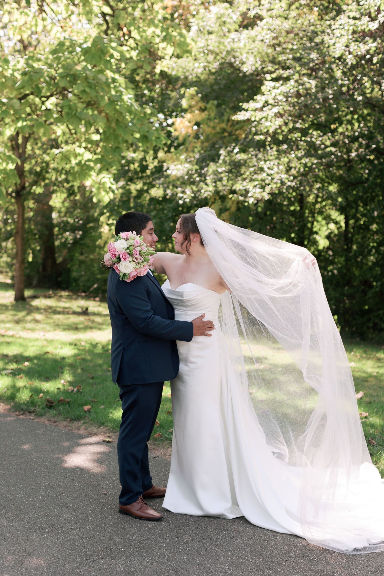A romantic wedding portrait with flowing veil in a sunlit garden setting.