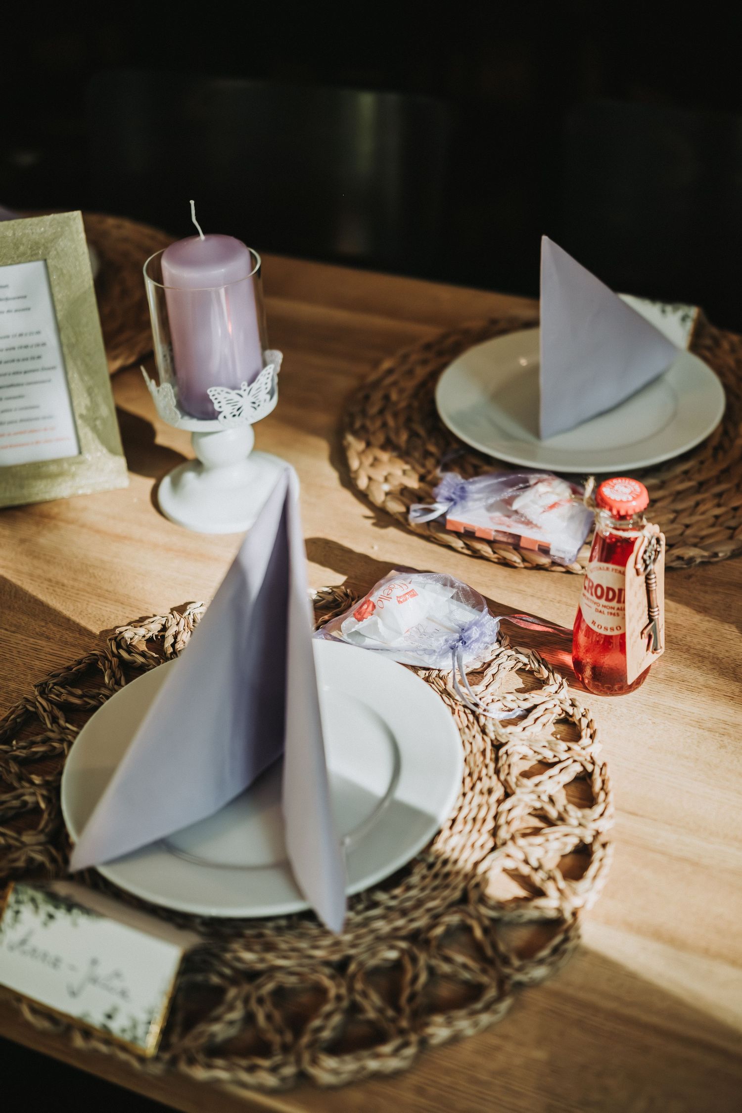 Rustic table setting with pink candle, folded napkins, and glass bottles on woven placemats.