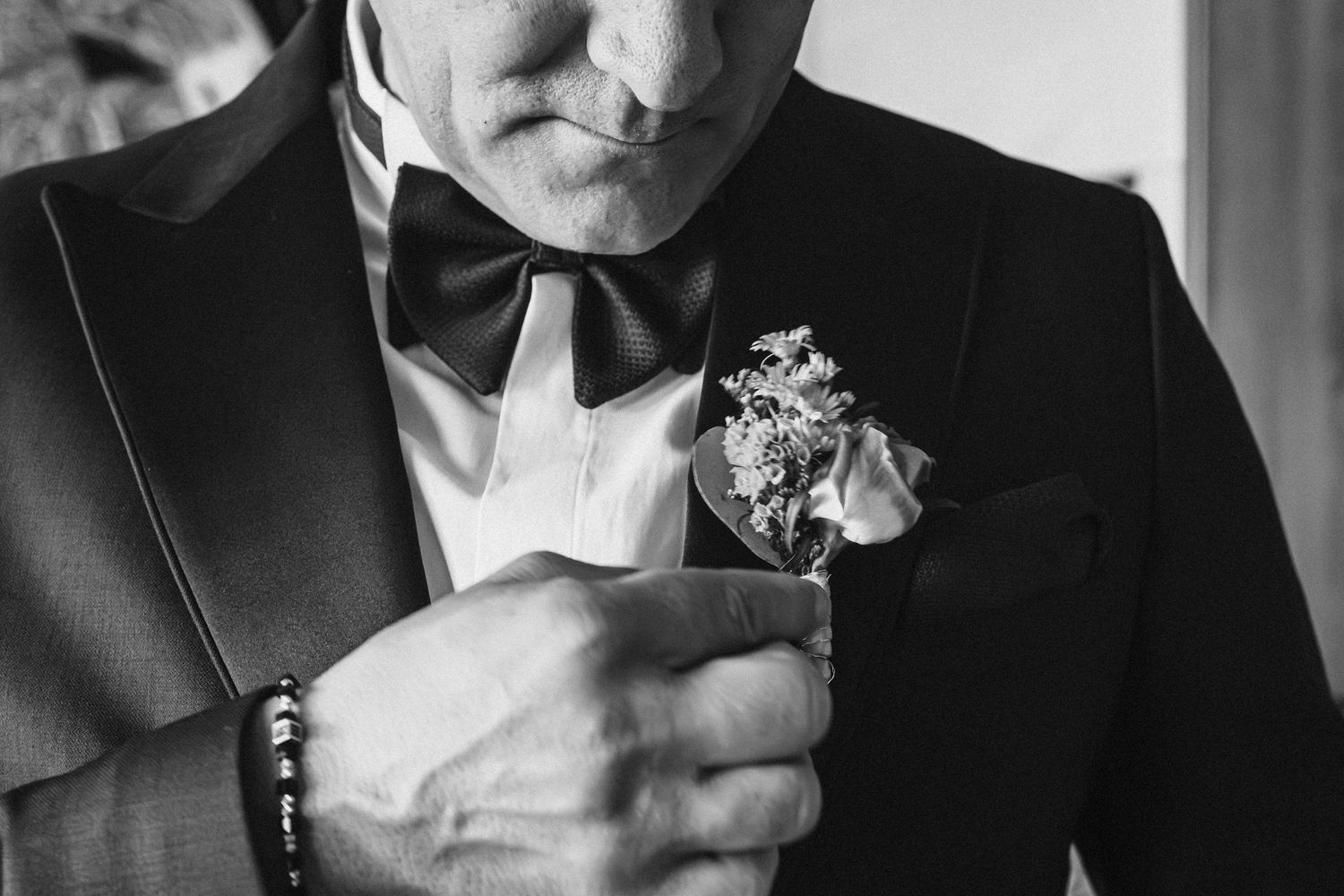Close-up of boutonniere and bowtie on classic black tuxedo jacket.